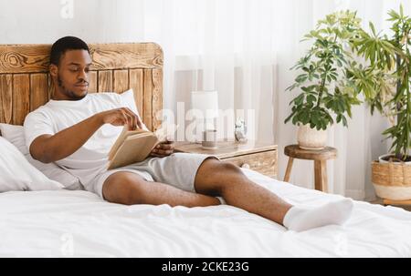 African American Man Reading Book Lying In Bed At Home Stock Photo