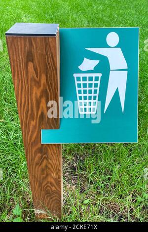 Sign of throw the trash in the trash can on background of green grass in park. Symbol on metallic plate. Stock Photo