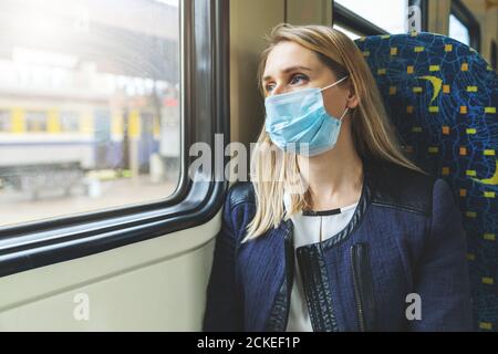 woman with safety face mask sitting in train and looking through the window. virus pandemic Stock Photo