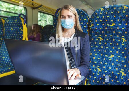 young woman with face mask using laptop in train public transport. virus pandemic Stock Photo