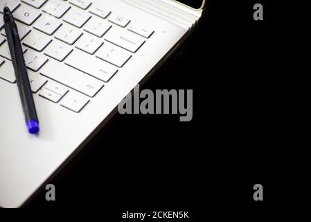 close-up of a pen lying down on laptop keypad against black background Stock Photo