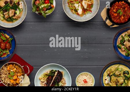 A border of bowls of delicious asian food, curries, chicken chow mein noodles, balti dishes, vegetable curries, on a dark wooden background with space Stock Photo