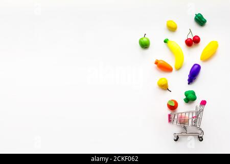 Concept of food and diet. Mini toy organic fruits and vegetables falling into mini shopping cart. Organic market concept Stock Photo