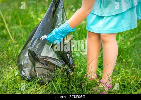 Child collects plastic trash from grass throwing garbage in garbage bag in the park Stock Photo