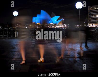 A group of women visiting Sydney's waterfront walk past the Sydney Opera House illuminated in a shade of blue October 24, 2015. Around 200 iconic monuments, buildings, museums, bridges and other landmarks in nearly 60 countries including Australia's architectural icon, will be lit up blue, the official colour of the United Nations, as part of a global campaign to commemorate its 70th anniversary.  REUTERS/Jason Reed