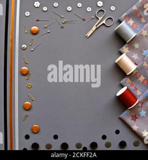 A birds eye flatlay of sewing accessories with cotton, material, scissors, safety pins, ribbons and buttons on a grey background. Stock Photo