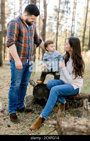 Family walk in the autumn forest. Pretty young mother and her little son sitting on an old log of a fallen tree and having fun with their handsome Stock Photo