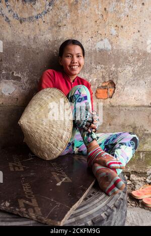 Can Tho / Vietnam - January 28, 2020: portrait of vietnamese young woman with traditional hat on arm sitting leaning on wall Stock Photo