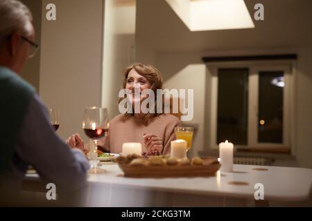 Happy senior woman sitting at the table and talking to her husband during dinner at home Stock Photo