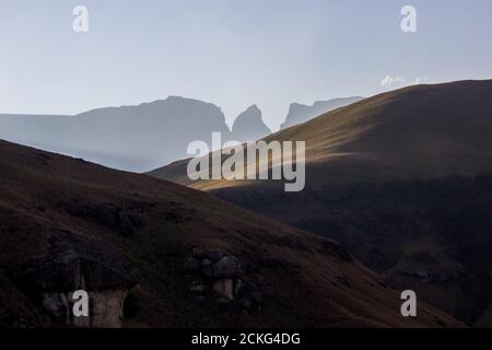 Last light on the grass covered slopes of the central Drakensberg Mountains of South Africa, with Monk’s Cowl and Champagne Castle in the Background Stock Photo