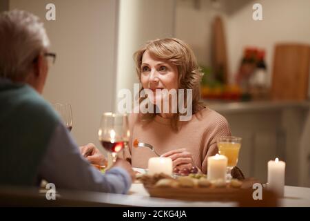 Mature woman listening to her husband while they having dinner at the table at home Stock Photo