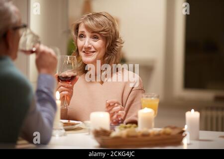 Smiling mature woman talking to man eating meal and drinking wine at the table at home Stock Photo