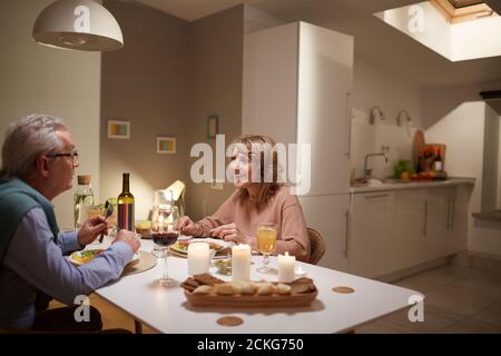 Happy senior couple sitting at the table in domestic kitchen they have festive dinner Stock Photo