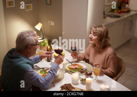 Senior people drinking red wine while sitting at the dining table during dinner at home Stock Photo