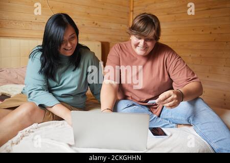 Two smiling women sitting on bed and using laptop for online shopping they paying by credit card Stock Photo