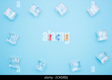 The word ICE on a blue background of wooden multicolored letters, ice cubes around the word. Stock Photo