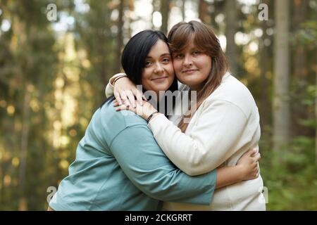 Portrait of two young lesbians embracing each other and smiling at camera while standing in the forest Stock Photo