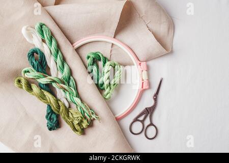 Set for embroidery. Linen fabric, patterns for embroidery, hoop, green thread and needles. Copy space, top view Stock Photo