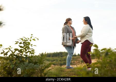 Overweight lesbians holding hands and dancing on the top of the hill outdoors Stock Photo