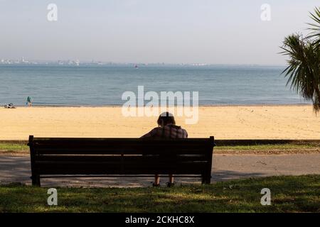 a woman sitting alone on a bench at the seaside or beach, Ryde, Isle of Wight Stock Photo