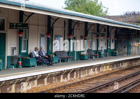 Two elderly men sitting on a bench on a train station platform waiting for a train to arrive