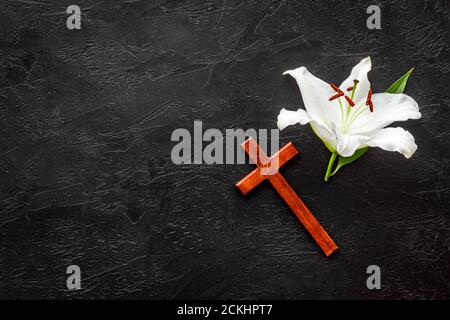 Funeral lily flowers with cross on dark stone background. Mourning symbols Stock Photo