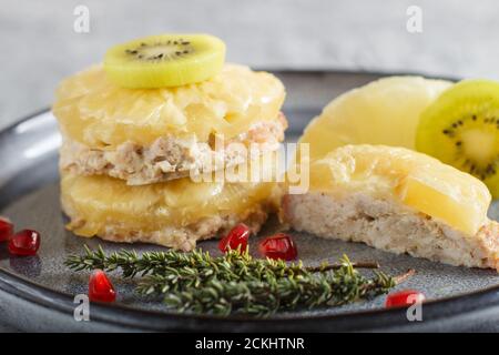 Pieces of baked pork with pineapple, cheese and kiwi on gray plate, side view, close up, selective focus. Stock Photo