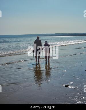 An old couple paddling in the sea on the beach at Filey Cobble Landing, North Yorkshire east coast, northern England, UK