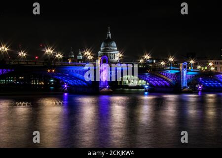 Southwark Bridge by night - A calm River Thames reflects the bright lights on Southwark Bridge, with St Paul's Cathedral in the background Stock Photo