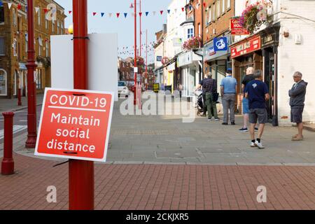 Daventry, Northamptonshire - 16/09/20: A queue of people behind a Covid-19 sign reminding them to maintain social distance. Stock Photo