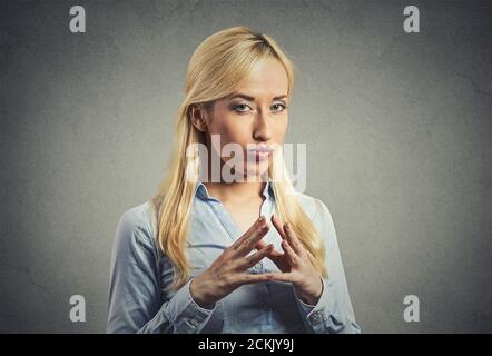 Closeup portrait sneaky, sly, scheming young woman plotting revenge plan, prankster isolated on gray wall background. Negative human emotion facial ex Stock Photo