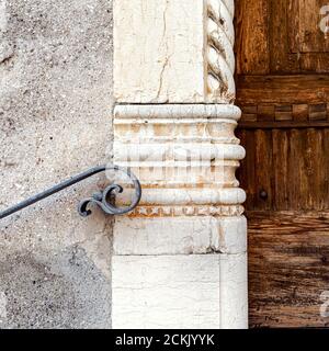 Exterior wall with detail of old wrought iron handrail with the stylized shape of a flying person. Ancient marble decoration. An ancient wooden door Stock Photo