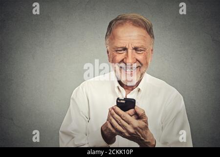 Smiling elderly man looking at his smart phone while text messaging isolated on gray wall background Stock Photo