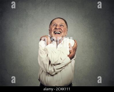 Closeup portrait confident smiling man holding hugging himself isolated on grey wall background. Positive human emotion, facial expression, feeling, r Stock Photo