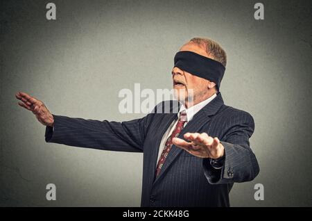 Portrait senior business man in suit blindfolded stretching his arms out isolated on gray wall background Stock Photo