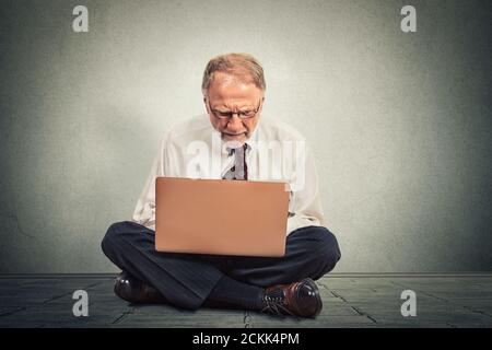 Business man thinking and sitting on the floor working on computer isolated on gray wall background Stock Photo