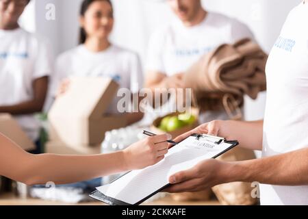 Selective focus of woman writing on clipboard near volunteer in charity center Stock Photo