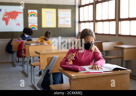 Girl wearing face mask studying while sitting on her desk at school Stock Photo