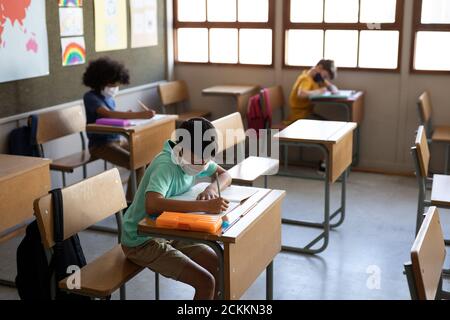 Group of kids wearing face masks writing while sitting on their desk at school Stock Photo