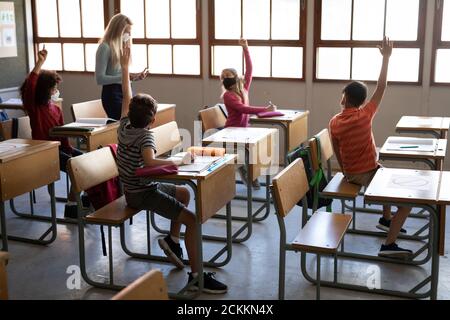 Group of kids wearing face masks raising their hands in the class Stock Photo