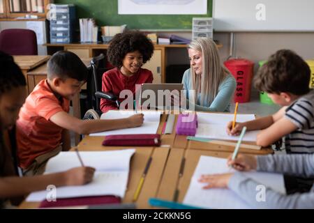 Female teacher with digital tablet teaching a disable boy in wheel chair at school Stock Photo