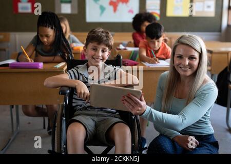 Portrait of female teacher and disable boy smiling while sitting in his wheelchair in class Stock Photo