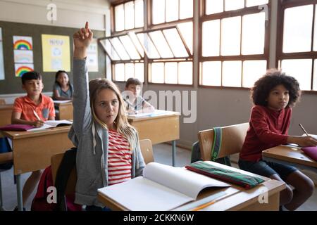 Girl raising her hand while sitting on her desk at school Stock Photo ...