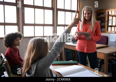 Girl raising her hand while sitting on her desk at school Stock Photo