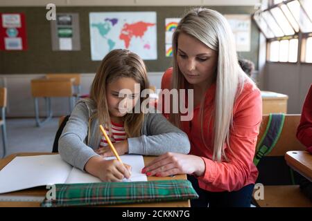 Female teacher helping a girl to write in a book in class at school Stock Photo