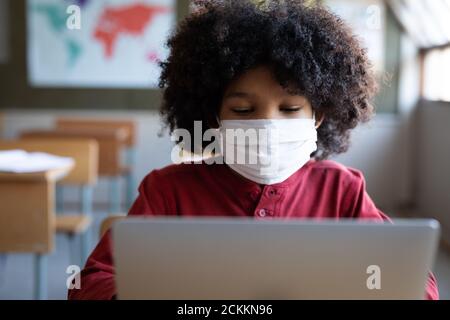 Boy wearing face mask using laptop on his desk at school Stock Photo
