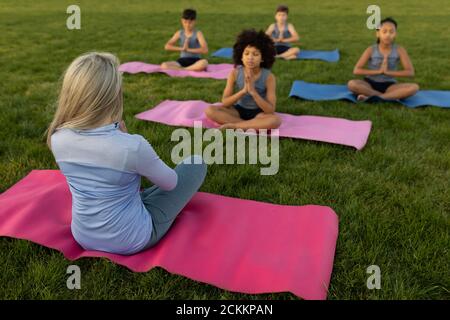 Female teacher and group of kids performing yoga in the garden Stock Photo