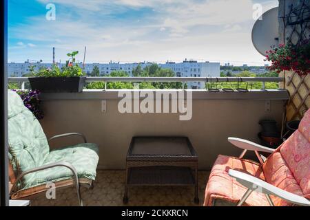 Modern interior of lounge zone on balcony in luxury apartment. Cozy chairs and coffee table. View of city at sunny summer day. Stock Photo