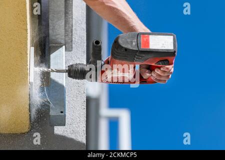 Working power hammer drill. Anchoring a steel construction. Fixing  into building masonry. Hand holding cordless drilling machine. Falling dust detail. Stock Photo
