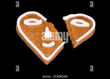 Broken heart from baked gingerbread decorated by smiley isolated on a black background. Smiling emoticon divided into two parts. Symbolic end of love. Stock Photo